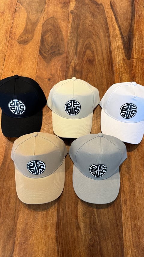 Five baseball caps in different colors arranged on a wooden surface, each featuring a circular logo design on the front